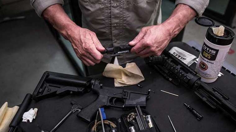 Male cleaning the bolt of an AR-style rifle with all of the parts laid out