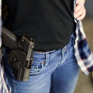 lower half of woman carrying concealed pistol under shirt in outer waist band holster