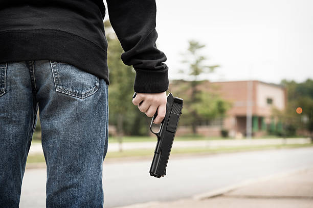 Adolescent male with pistol in hand standing and looking at a school