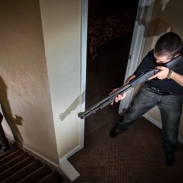Homeowner with shotgun at top of stairs with armed burgler coming up the stairs